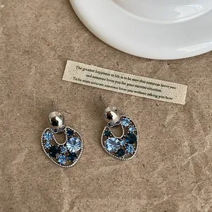 Primo piano di orecchini a lobo geometrici con strass blu su sfondo strutturato.
