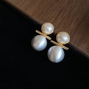 Close-up of brushed silver and gold earrings with white pearl accents on black velvet