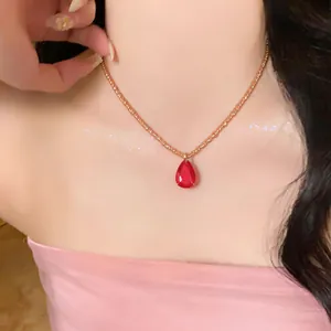 Vue détaillée d'un collier de perles dorées avec pendentif goutte rouge sur un modèle.