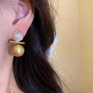 Detailed close-up of 18k gold plated brushed metal earrings with pearl inlay worn on ear