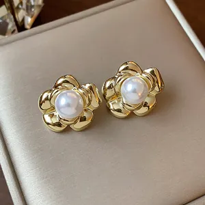 Close-up of gold-plated flower stud earrings with elegant central pearl on display.