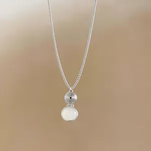 Macro detail of an ethnic silver necklace with spiral textured disc and white resin pendant