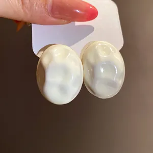Close-up of minimalist cream oval earrings featuring a unique crinkled texture detail.