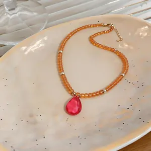 Gros plan d'un collier de perles orange avec un pendentif en cristal en forme de goutte rose.