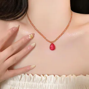 Gros plan d'un pendentif goutte d'eau rouge sur un collier de perles orange.