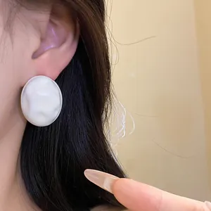 Close-up of a minimalist white wrinkled oval stud earring shown on a model ear lobe