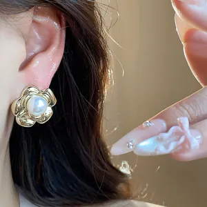 Close-up shot of a gold-plated flower pearl stud earring worn on an ear with nail art