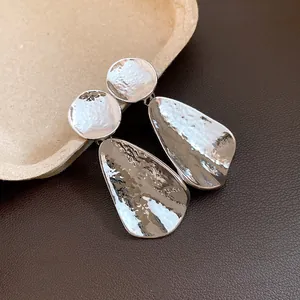 Dettaglio di orecchini a goccia d'argento con trama martellata e design minimalista moderno