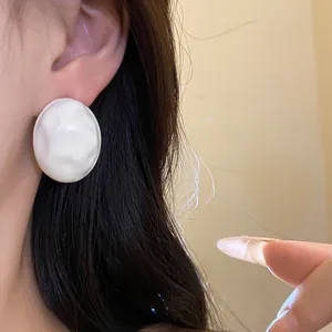 Close-up detail of a minimalist white crumpled oval stud earring shown on a model