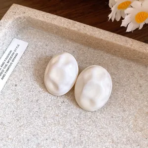 Close-up of minimalist white oval earrings with a crumpled texture on a stone tray.