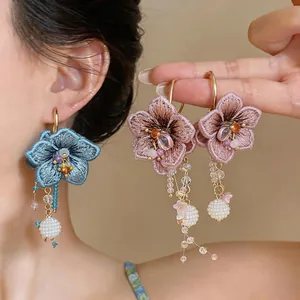Detailed view of handmade embroidered flower earrings with elegant glass tassels on a model.