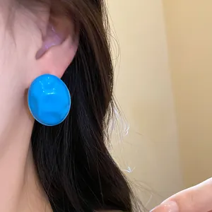 Close-up view of a vibrant blue oval stud earring with a unique crumpled texture design