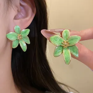 Gros plan sur d'élégantes boucles d'oreilles fleurs en émail vert vintage et doré.