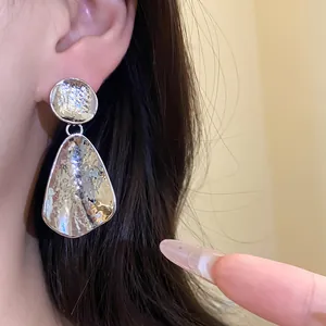 Primo piano dei dettagli degli orecchini a goccia in argento martellato indossati dal modello