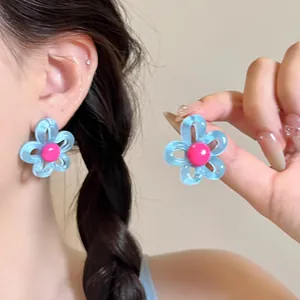 Detailed macro view of blue hollow flower earrings with pink center on model's ear