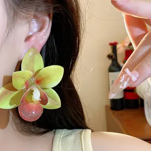 Detailaufnahme eines großen grünen Orchideen-Ohrsteckers, getragen von einem Modell.