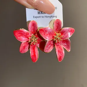 Gros plan de boucles d'oreilles fleurs en émail rose avec pétales bordés d'or et vintage.