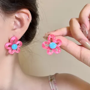 Close-up of vibrant pink hollow flower stud earrings with a bright blue center piece