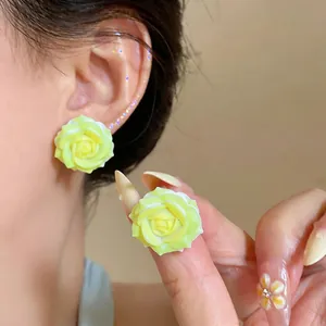 Detailed view of handmade yellow resin rose stud earrings shown on ear and held by hand