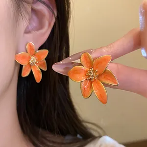 Gros plan de boucles d'oreilles fleurs en émail orange vintage avec centre doré.
