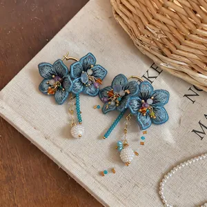 Detail view of handmade blue embroidered flower earrings with glass bead tassels and pearls.
