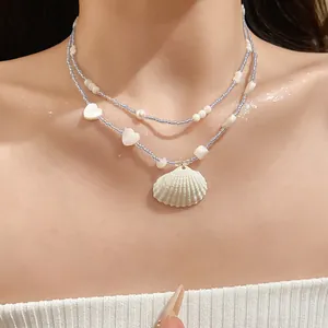 Close-up of beach summer blue beaded necklace featuring white shell and heart charms