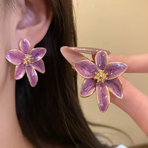 Vue rapprochée détaillée d'élégantes boucles d'oreilles fleurs en émail violet portées et tenues