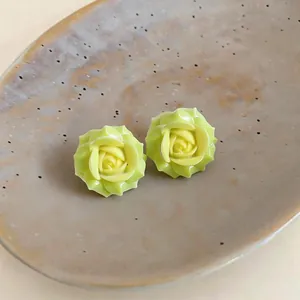 Close-up of light green resin flower stud earrings on a ceramic tray