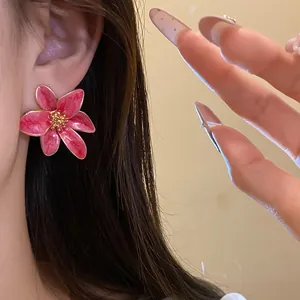 Vue macro détaillée d'élégantes boucles d'oreilles fleur en émail rose et doré sur modèle
