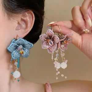 Close-up view of handmade embroidered flower earrings with elegant glass tassel details.