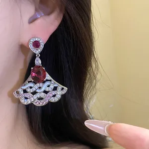 Close-up of elegant fan-shaped zircon drop earrings with red oval gemstones on model.