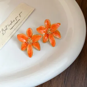 Gros plan détaillé des boucles d'oreilles fleurs orange avec bordure dorée sur plateau