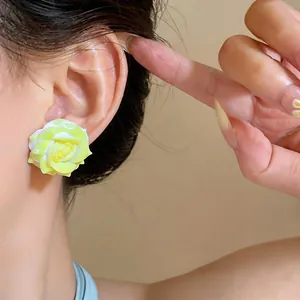 Detailed view of elegant yellow resin rose flower stud earrings on an ear model
