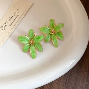 Vue détaillée de boucles d'oreilles fleurs en émail vert avec bordure dorée sur plateau