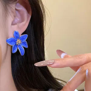Gros plan d'une boucle d'oreille fleur en émail bleu avec un centre doré texturé