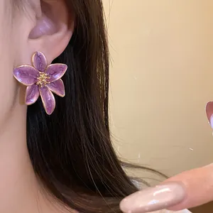 Détail d'une boucle d'oreille fleur en émail violet de style vintage portée par un modèle