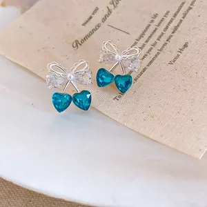 Dettaglio macro di orecchini a fiocco con cuore blu ghiaccio e accenti di perle.