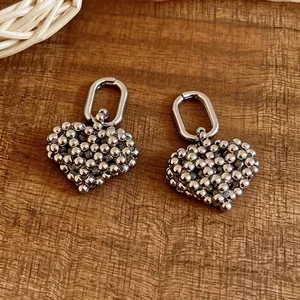 Elegant silver-toned beaded hollow heart hoop earrings on a rustic wood surface
