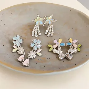 Macro detail of three pairs of floral and star-shaped zircon earrings on a ceramic dish