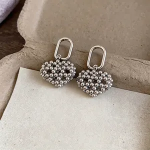 Elegant silver-toned earrings featuring unique beaded hollow heart charms on oval hoops