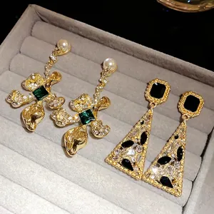 Vintage gold drop earrings set with emerald green and black crystals in jewelry tray.