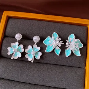 Dettaglio di orecchini a fiore e quadrifoglio in smalto verde menta con perle e zirconi.
