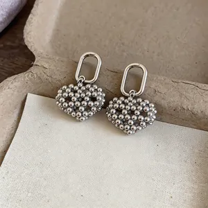 Detail shot of silver beaded openwork heart earrings on a textured paper background