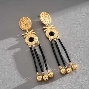Macro detail of vintage gold portrait earrings with black tassels and Greek key design