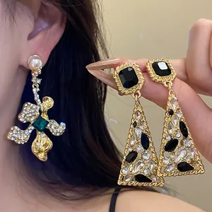 Close-up detail of luxury vintage floral and triangular gold dangle earrings with crystals