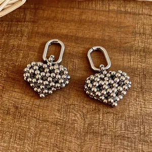 Detail of silver beaded heart charm earrings on a rustic wooden background.