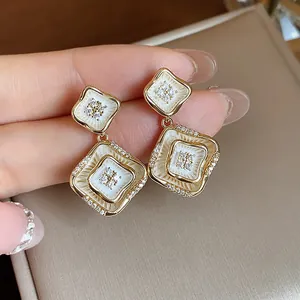 Nahaufnahme der 18 Karat vergoldeten Rautenohrringe mit weißem Emaille und Zirkonia.