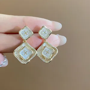 Nahaufnahme von 18 Karat vergoldeten Rautenohrringen mit Zirkonia-Inlays und weißer Emaille