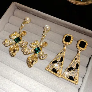 Close-up of vintage gold earrings with emerald green and black stones in a grey tray