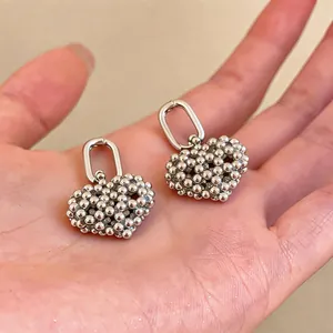 Close-up detail of exquisite silver beaded heart hoop earrings held in hand for scale